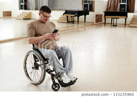 High angle view of mature man in wheelchair scrolling social media page on smartphone during break at dance class 113235960
