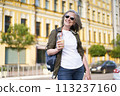 A female pedestrian strolling on the street while holding a beverage in her hand. 113237160