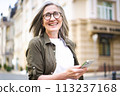 A woman wearing glasses is holding a cell phone in her hand. 113237168