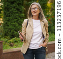 A woman with glasses wearing a tan blazer. 113237196