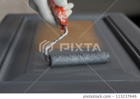 Person remonier paints a wooden product, kitchen facade with a roller with gray paint or primer. 113237646