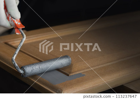 Person remonier paints a wooden product, kitchen facade with a roller with gray paint or primer. copy space 113237647