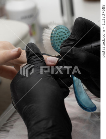 Beauty concept. A manicurist in black latex gloves gives a hygienic manicure to a client in a beauty salon. Close-up. Vertical. Beauty concept. A manicurist in black latex gloves gives a hygienic manicure to a client in a beauty salon. Close-up. Vertical. 113237688