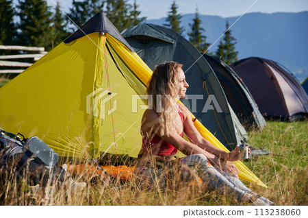 Woman traveller camping in mountains. Tourist sitting in campsite, admiring landscape with cup of tea. Sporty, young female having break, looking, enjoying. Concept of beauty of nature. 113238060