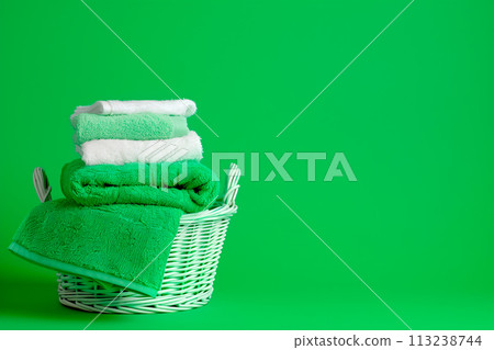 Stack of clean towels in laundry wicker basket on green background. The towels showcasing their soft and fluffy textures 113238744