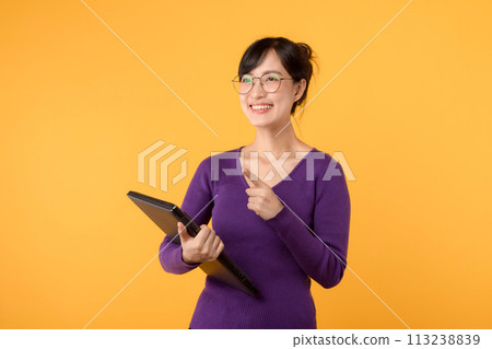 Happy asian female college student or teacher happy smiling on yellow background, holding laptop. Youth girl student pointing up to copy space. Education exchange student concept 113238839