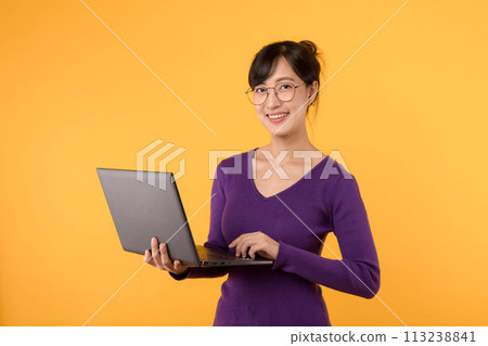 Portrait young asian woman student wearing purple shirt and eyeglasses happy smile holding laptop isolated on yellow background. education, businesswoman model concept. 113238841