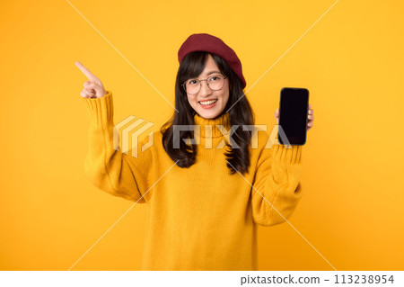 Yellow themed online joy. Woman in a red beret and yellow sweater uses her smartphone while celebrating online success. 113238954