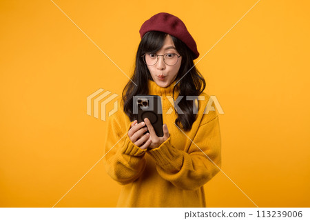 Portrait young Asian woman 30s wearing yellow shirt and glasses receive an exited news from mobile phone isolated on yellow background. Great news concept. 113239006