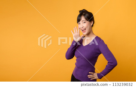 Portrait young beautiful 30s asian woman happy smile dressed in purple clothes shout to free space isolated on yellow studio background. Presenting product Beautiful girl act like telling to customer. 113239032