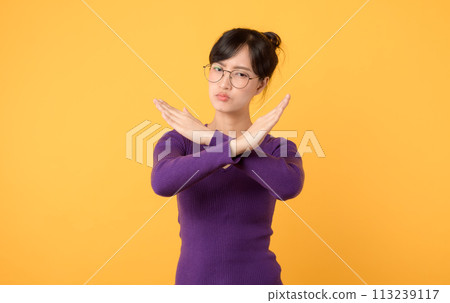 portrait young lady wearing a purple shirt and eyeglasses, using X gesture with arms, indicating negative or forbidden action. Seriousness and caution evident expression against a yellow background. portrait young lady wearing a purple shirt and eyeglasses, using X gesture with arms, indicating negative or forbidden action. Seriousness and caution evident expression against a yellow background. 113239117
