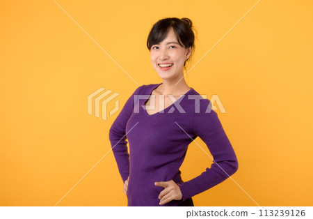 A cheerful young woman wearing a purple shirt and eyeglasses, in a studio portrait, displaying confidence and positivity against a vibrant yellow background. 113239126