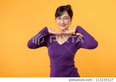 Portrait of a pretty and confident female model wearing a purple shirt and eyeglasses, showcasing modern beauty and elegance against a vibrant yellow background. 113239127