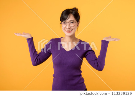 Showing young business woman 30s with open hand palms for copy space for two products. Businesswoman in purple shirt with glasses isolated on yellow background. Choose best deal advertising concept. Showing young business woman 30s with open hand palms for copy space for two products. Businesswoman in purple shirt with glasses isolated on yellow background. Choose best deal advertising concept. 113239129