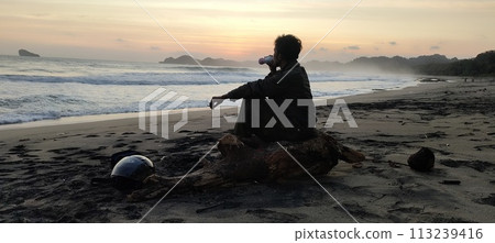 A man relaxing on the beach alone while enjoying the beauty of the outdoors A man relaxing on the beach alone while enjoying the beauty of the outdoors 113239416