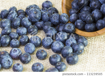 Blueberries in a wooden bowl scattered on a rustic table 113239585