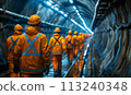 Workers in hard hats walk through a round tunnel. 113240348
