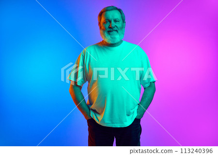 Portrait of bearded man wearing polo shirt, standing with calm relaxed face and looking at camera on gradient blue-purple background in neon light Portrait of bearded man wearing polo shirt, standing with calm relaxed face and looking at camera on gradient blue-purple background in neon light 113240396