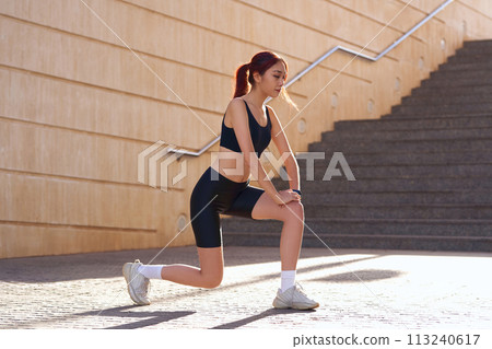 Athletic woman in sportswear stretching legs before doing workout outside in morning 113240617
