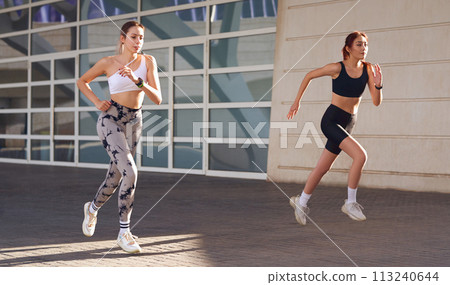 Two active women athlete running on sunny morning side by side on modern buildings background 113240644