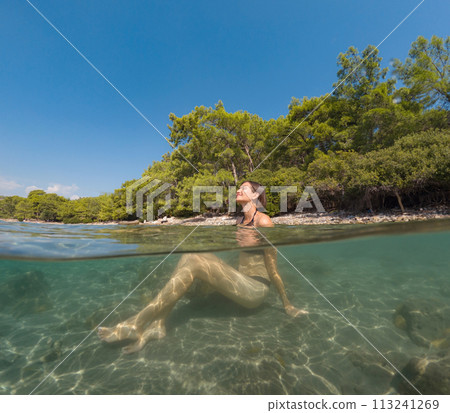 Young female on holidays enjoy floating on a crystal clear water beach of Antalya Turkey. Asian beautiful woman swimming with open arms. Relax and tranquility. Travel and Holiday concept. 113241269