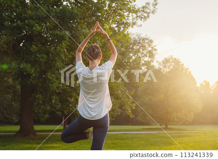 Young asian woman doing yoga in morning or evening at park, healthy woman relaxing and practicing tree pose at city park. Mindfulness, destress, Healthy habits and balance concept Young asian woman doing yoga in morning or evening at park, healthy woman relaxing and practicing tree pose at city park. Mindfulness, destress, Healthy habits and balance concept 113241339