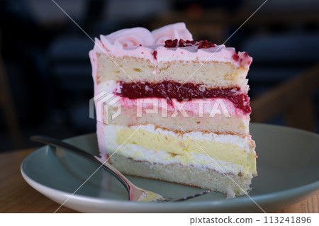 Eating cheesecake with a fork. Taking bite of cheesecake. Sweet dessert food Close up of a pink strawberry cake swirling on a white plate. 113241896