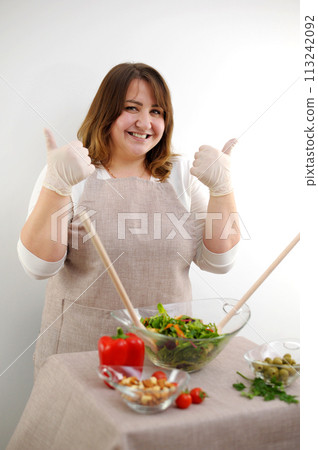 Cheerful female chef is sitting at the table with bunch of vegetable, showing prepared meal and ok sign.Female chef showing prepared meal and ok sign  113242092