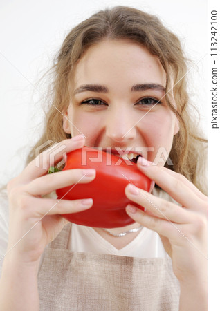 funny cheerful teen girl young woman biting red pepper healthy eating delicious food cooking salad sincerely sly look smile beautiful teeth brown hair apron kitchen close-up delicate manicure health 113242100