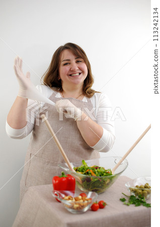 beautiful plump woman cook food concept of cleanliness neatness healthy attitude ingredients are on table wooden spoons in glass bowl will knead salad sincere smile place for text beautiful plump woman cook food concept of cleanliness neatness healthy attitude ingredients are on table wooden spoons in glass bowl will knead salad sincere smile place for text 113242134