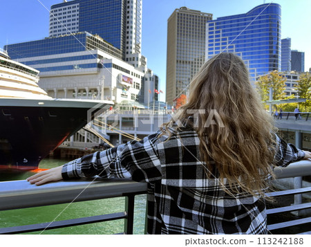 A young girl looks at the sea on a huge cruise liner that is sailing off the coast of Canada Place Center Vancouver and skyscrapers are also visible she is in a black plaid shirt her hair is loose A young girl looks at the sea on a huge cruise liner that is sailing off the coast of Canada Place Center Vancouver and skyscrapers are also visible she is in a black plaid shirt her hair is loose 113242188