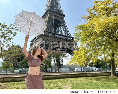 a beautiful young girl in a summer dress stands against the backdrop of the Eiffel Tower with a lace umbrella, she raised her hand and as if taking off there is a place for advertising travel agency a beautiful young girl in a summer dress stands against the backdrop of the Eiffel Tower with a lace umbrella, she raised her hand and as if taking off there is a place for advertising travel agency 113242218
