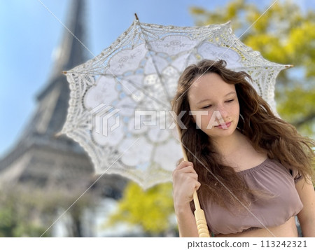 a girl with a white parasol stands against the backdrop of the Eiffel Tower with her back to us can be used for advertising for the Internet for travel agencies 113242321