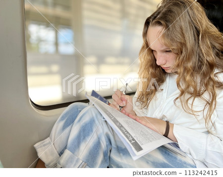 European girl with blond long hair in a white shirt rides in skytrain teenage girl diligently does her homework to hold a notebook on her knees through the window and goes home she is 13-15 years old European girl with blond long hair in a white shirt rides in skytrain teenage girl diligently does her homework to hold a notebook on her knees through the window and goes home she is 13-15 years old 113242415
