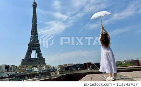 a beautiful young girl in a summer dress stands against the backdrop of the Eiffel Tower with a lace umbrella, she raised her hand and as if taking off there is a place for advertising travel agency a beautiful young girl in a summer dress stands against the backdrop of the Eiffel Tower with a lace umbrella, she raised her hand and as if taking off there is a place for advertising travel agency 113242417