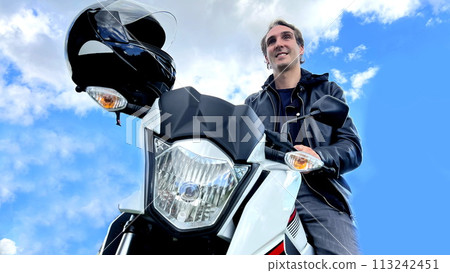 male biker sits on a motorcycle against the background of nature and mountain he in a leather jacket on the handlebars of a motorcycle is wearing a helmet male biker sits on a motorcycle against the background of nature and mountain he in a leather jacket on the handlebars of a motorcycle is wearing a helmet 113242451