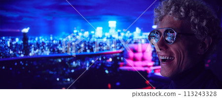 Happy young man standing outdoors in evening. Glasses reflecting fireworks and city lights 113243328