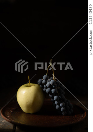 Blue grapes and green apple on a clay plate Blue grapes and green apple on a clay plate 113243489