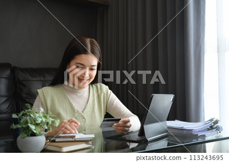Attractive young woman holding credit card and calculating monthly expenses at home 113243695