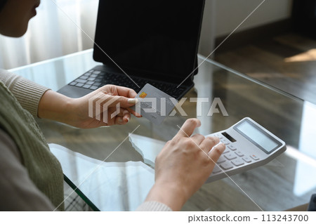 Attractive young woman holding credit card and calculating monthly expenses at home 113243700