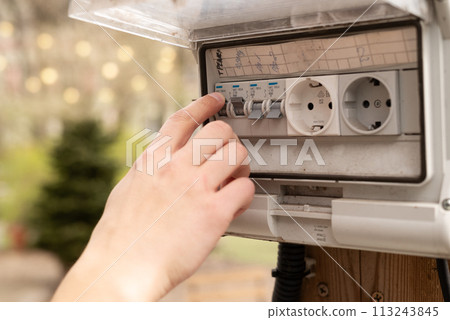 Man's finger checking an electricity in the fuse box outdoor. Block of sockets with a switch at the garden Man's finger checking an electricity in the fuse box outdoor. Block of sockets with a switch at the garden 113243845