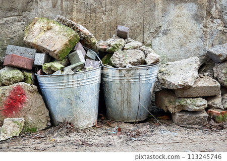 Old metal buckets among aged bricks filled with small broken brick pieces on abandoned construction site 113245746