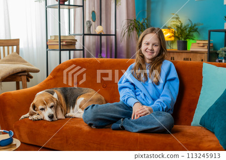 Portrait of smiling young girl animal lover with cute beagle dog sitting on orange sofa at home Portrait of smiling young girl animal lover with cute beagle dog sitting on orange sofa at home 113245913