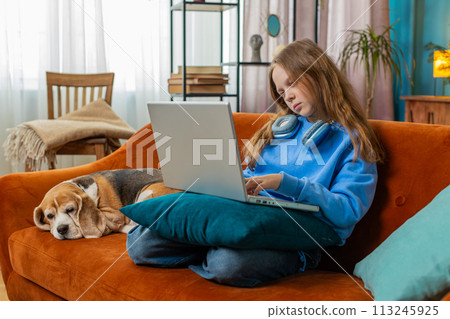 Overtired Caucasian teenage child girl bored using laptop doing a education project types lazily 113245925