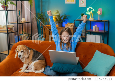 Happy child girl using laptop typing playing game good positive news celebrate online win at home Happy child girl using laptop typing playing game good positive news celebrate online win at home 113245945