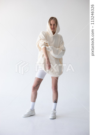 Beautiful blonde woman posing in white hoodie and leggings posing against white background 113246326