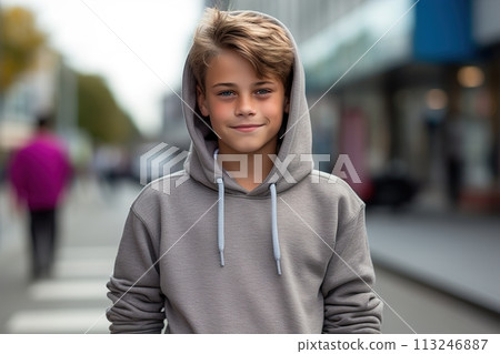 A young boy wearing a gray hoodie is smiling and standing on a street 113246887