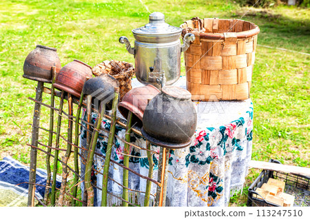 Vintage wicker handmade basket, samovar and utensils of pottery on table 113247510