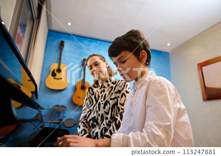 Talented teenager boy musician having a piano lesson with his teacher. Female pianist explaining the correct position of hands on piano keys 113247881