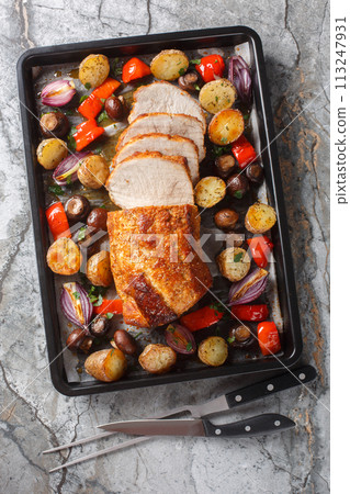 Festive baked pork loin with potatoes, onions, peppers and mushrooms close-up on a baking sheet. Vertical top view 113247931